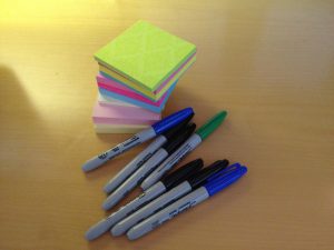A stack of Post-it notes and seven Sharpie markers