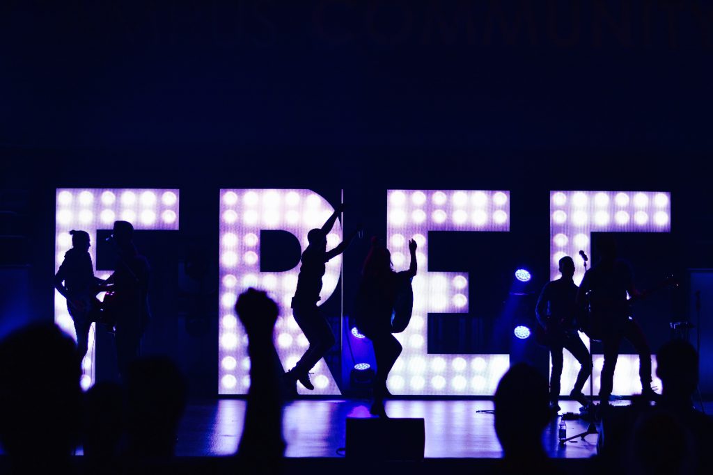 Dancers in silhouette in front of a large lighted sign with the word "FREE"